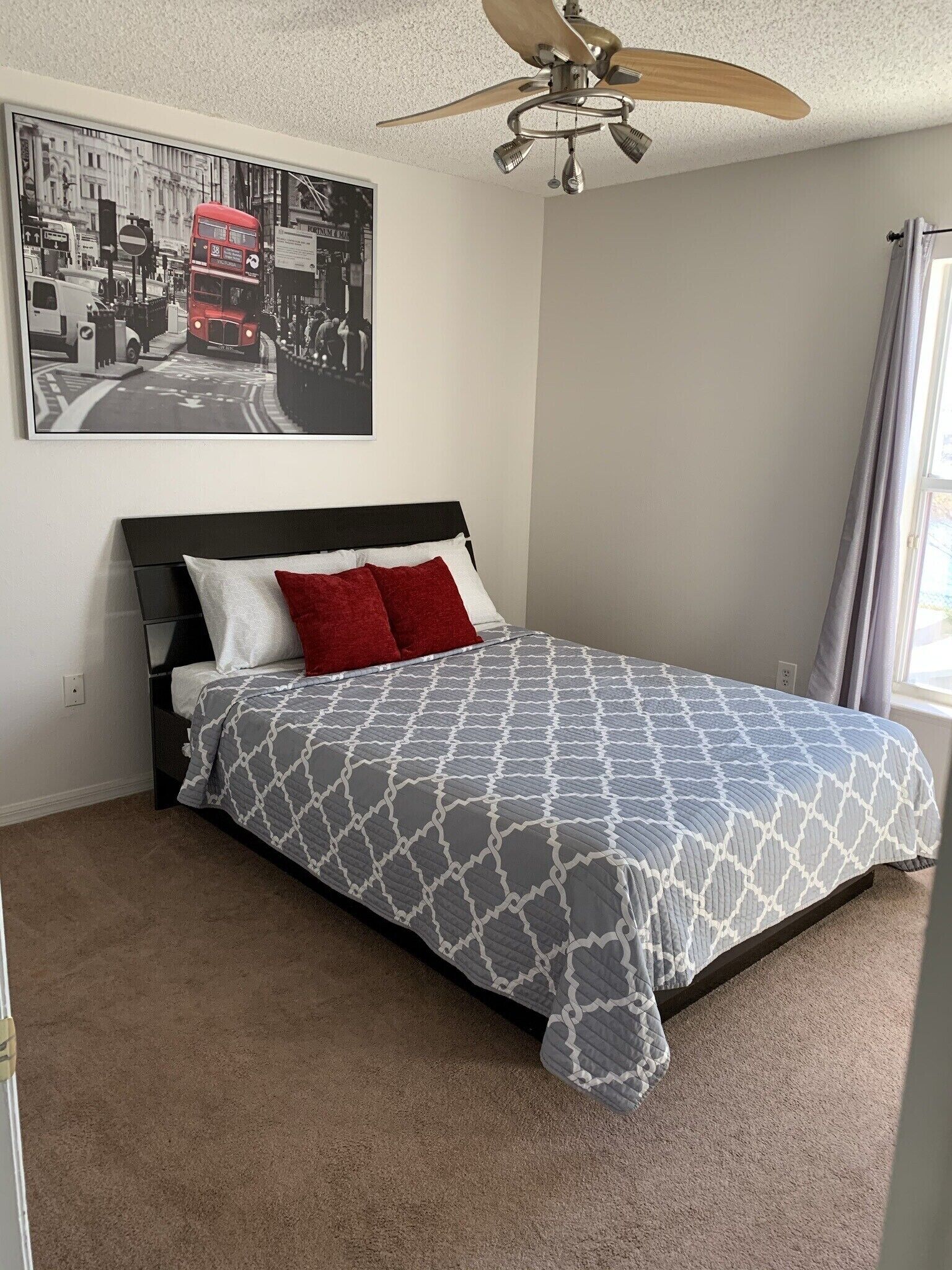Quarto com cama, ventilador de teto, pintura de paisagem urbana e janela com cortinas.
