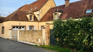 A two-story house with a sloped roof, a stone wall, and a metal gate. - Take a break "Au fil de l'ô (Moutiers-au-Perche)
