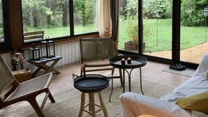 A cozy room with a large window, a wicker chair, a small table, and a cushioned sofa. - Take a break "Au fil de l'ô (Moutiers-au-Perche)