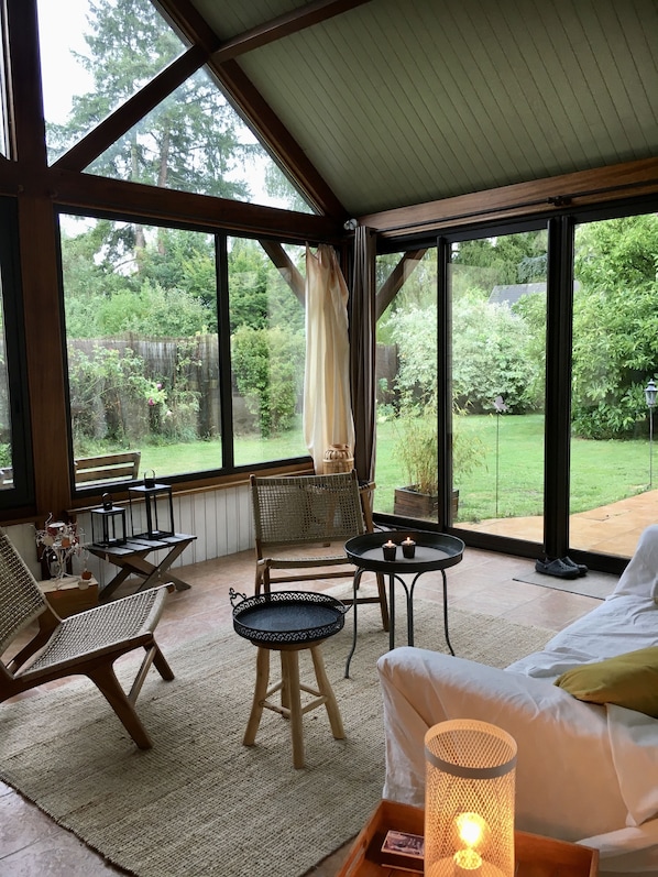 Una habitación acogedora con un ventanal grande, una silla de mimbre, una mesita pequeña y un sofá con cojines.
