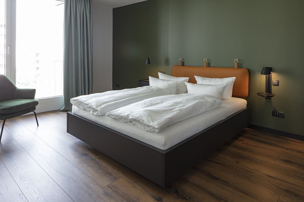 A modern bedroom with a large bed, a green wall, and a wooden floor.