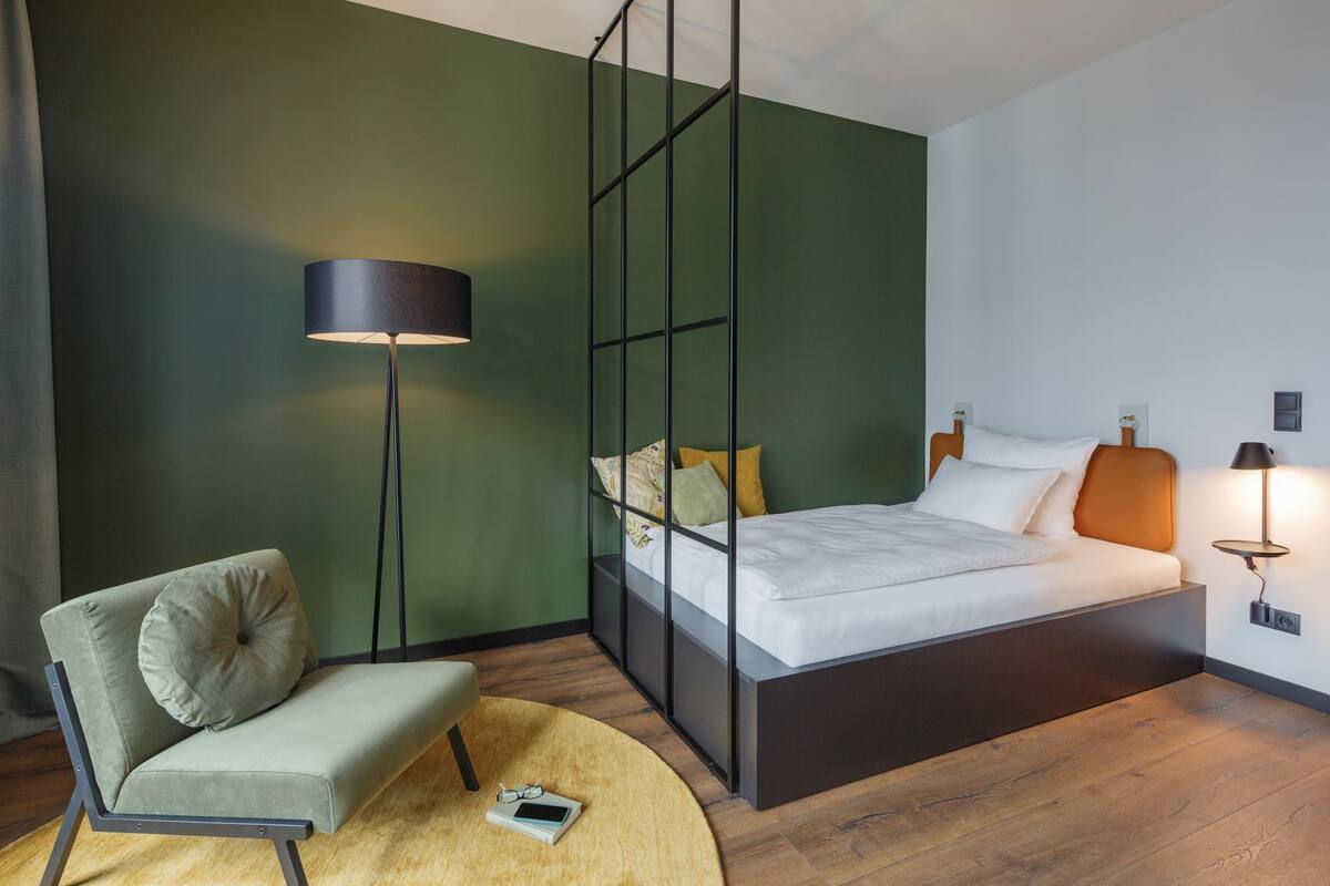 A modern bedroom with a bed, a chair, a floor lamp, and a bedside table.