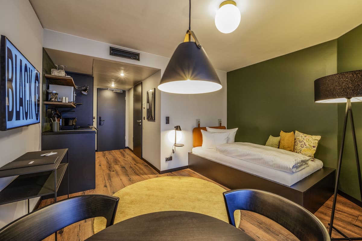 A modern hotel room with a bed, desk, chair, and a dining table.