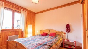 A wooden-paneled room with a bed, a nightstand, a lamp, and a window with curtains.
