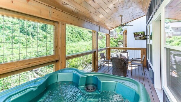 A wooden deck with a hot tub, large windows, and outdoor furniture. - Rushing Water/Hot Tub/Walk 2 Downtown Gatlinburg (Gatlinburg)