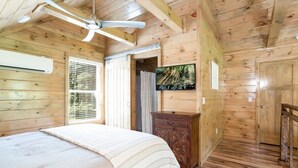 A wooden cabin bedroom with a bed, a ceiling fan, a wooden dresser, and a window with blinds. - Rushing Water/Hot Tub/Walk 2 Downtown Gatlinburg (Gatlinburg)