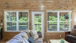 A cozy cabin interior with a brown leather couch, a wooden coffee table, and large windows with blinds. - Rushing Water/Hot Tub/Walk 2 Downtown Gatlinburg (Gatlinburg)