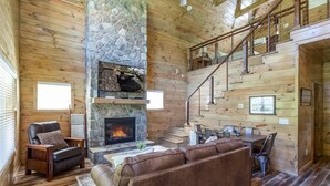 A cozy log cabin interior with a stone fireplace, leather furniture, and a wooden staircase. - Rushing Water/Hot Tub/Walk 2 Downtown Gatlinburg (Gatlinburg)