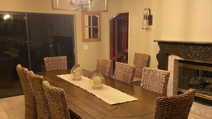 Een eetkamer met een grote houten tafel, rieten stoelen en een kroonluchter.