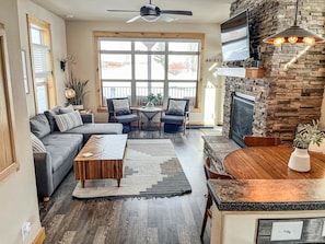 A living room with a sofa, coffee table, and chairs, a fireplace, and a dining area. - Edgewater Cabin on the Fraser River | 3BR Sleeps 7 | Kids Trout Pond & Pool (Granby)