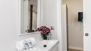 Un baño blanco con lavamanos, espejo y una planta en maceta con flores.