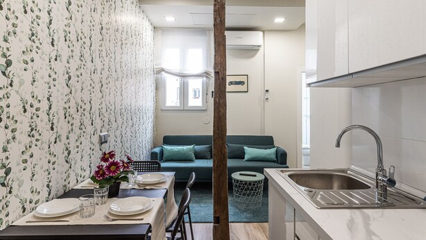 Una cocina moderna con un lavamanos, una mesa de comedor dispuesta con platos y vasos, y un sofá al fondo.