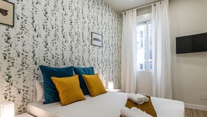 Habitación de hotel con cama, almohadas, mesita de noche, lámpara y ventana con cortinas.