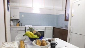 A kitchen with a white countertop, a stove, and cabinets. There are fruits, bread, and a coffee mug on the counter. - Collioure Town with Parking – Apartment Sorra (Collioure)