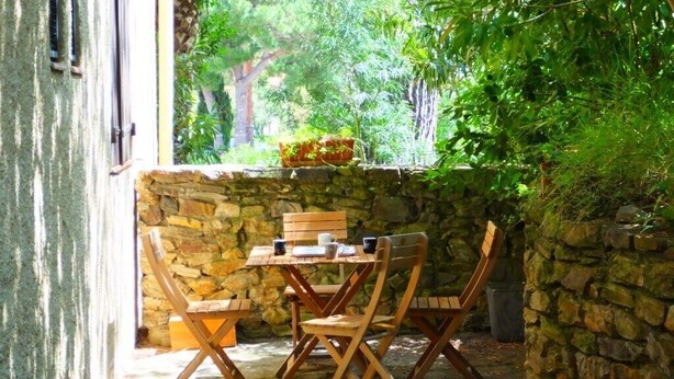 A stone wall with a table and chairs in a shaded outdoor area. - Collioure Town with Parking – Apartment Sorra (Collioure)