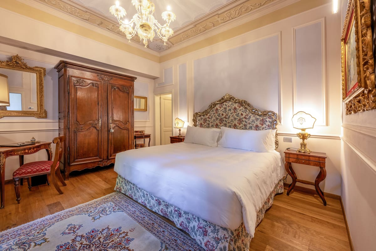 Een slaapkamer met een groot bed, een houten garderobe en een kroonluchter.