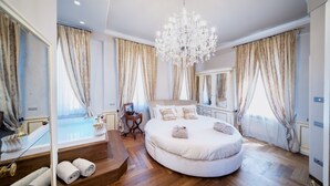 Une chambre à coucher luxueuse avec un lit rond, un lustre et de grandes fenêtres ornées de rideaux.