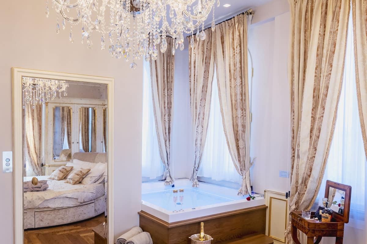 Een slaapkamer met een grote spiegel, een kroonluchter, een bed en een badkamer met een bad.