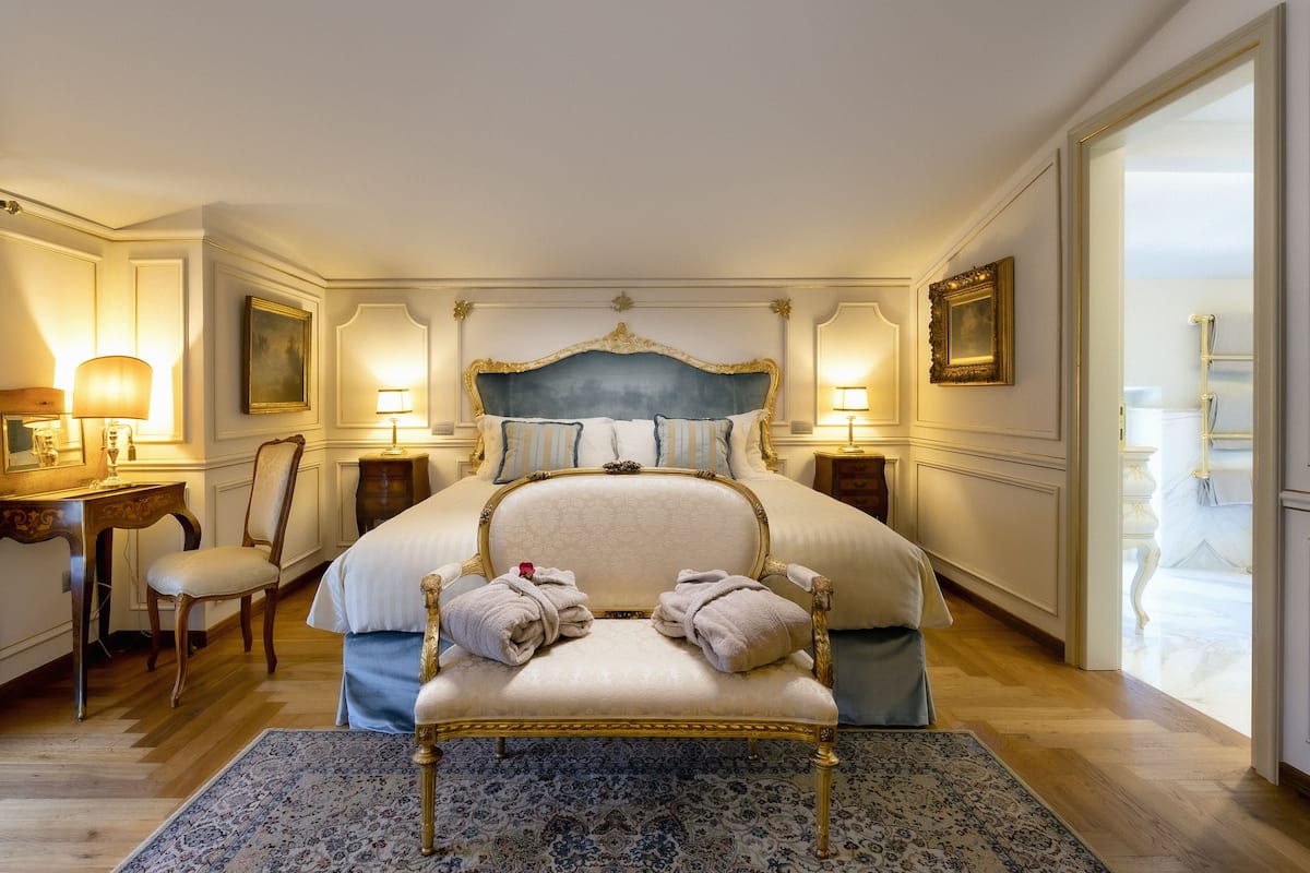 Een ruime slaapkamer met een groot bed, een fauteuil, een bureau en een spiegel.