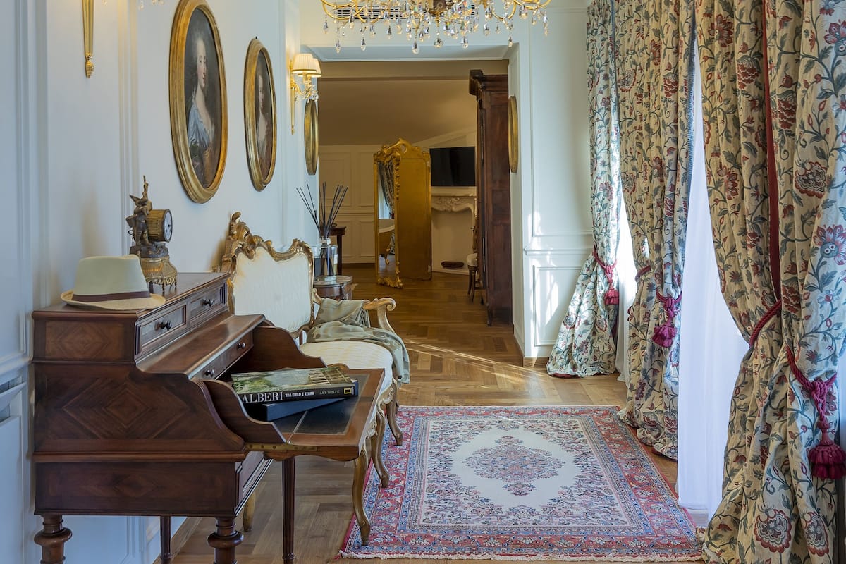 Een kamer met een houten piano, een bank, een kroonluchter en een kamerbreed tapijt met een patroon.