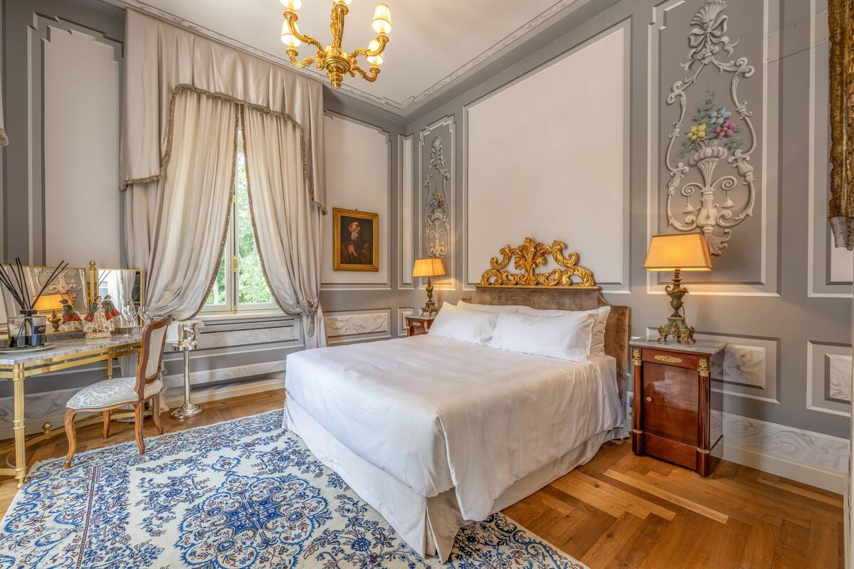 Een slaapkamer met een groot bed, een bureau met stoel, een raam met gordijnen en een decoratief wandobject.
