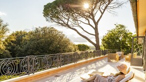 Un espace de détente extérieur, baigné de soleil, avec deux fauteuils inclinables et une table, offrant une vue sur un arbre et un ciel dégagé.