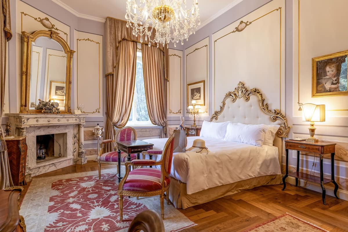 Een luxe slaapkamer met een groot bed, versierde meubels, een open haard en een kroonluchter.