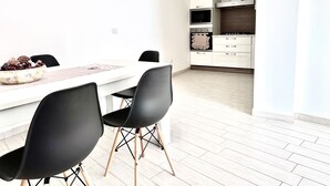 A modern kitchen with white cabinets, a stainless steel range hood, and a dining area with a white table and black chairs. - Appartamento Ibiscus (Cannigione)