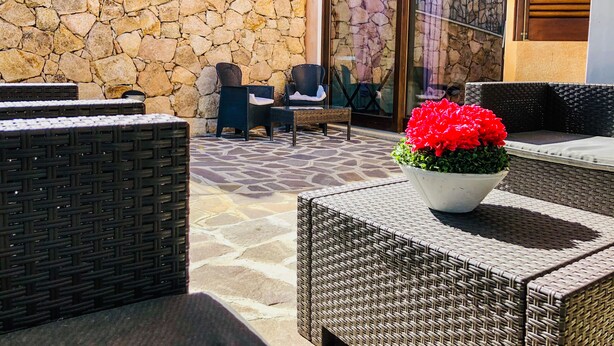 A patio area with wicker furniture, a stone wall, and a large window with a view of the interior. - Appartamento Ibiscus (Cannigione)