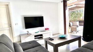 A modern living room with a flat-screen TV, grey sofas, a coffee table, and a sliding glass door leading to an outdoor area. - Appartamento Ibiscus (Cannigione)
