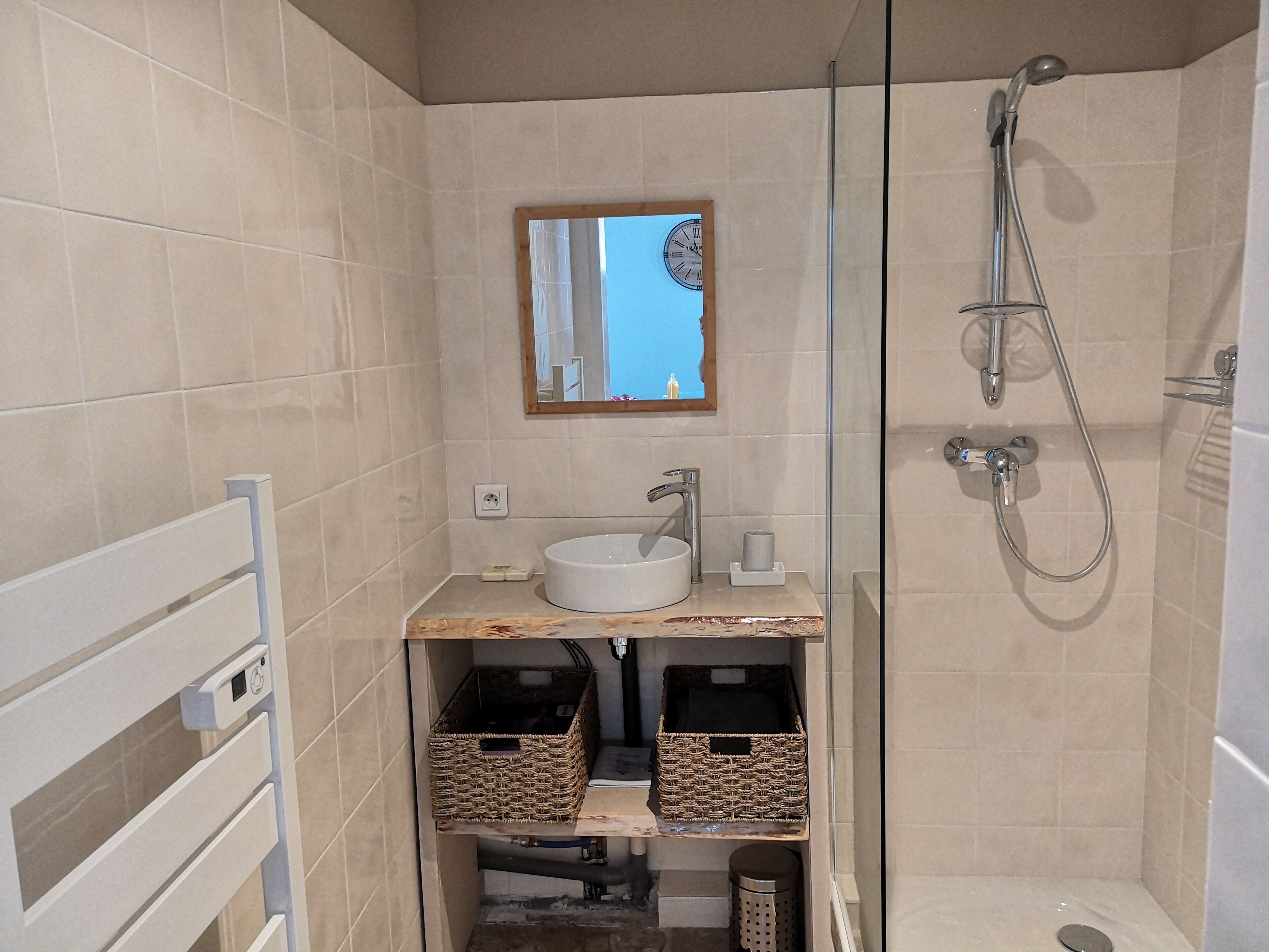 A bathroom with a glass-enclosed shower, a white sink, and a mirror above it. There are two wicker baskets under the sink.