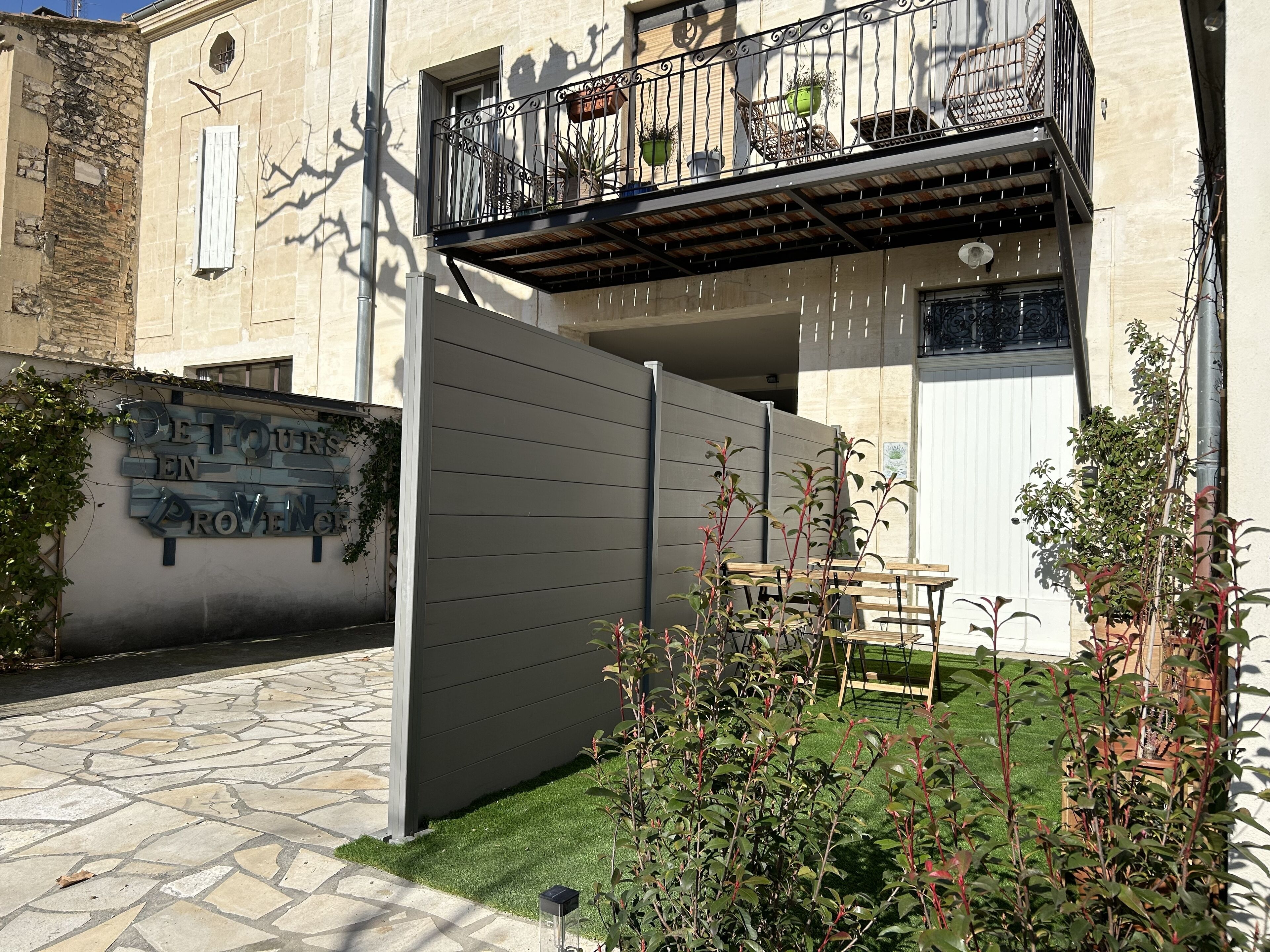 A residential building with a gated entrance, a balcony with potted plants, and a small patio area with a table and chairs.