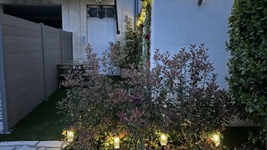 Ein Gartenbereich mit Topfpflanzen und einem Tisch, umgeben von einer niedrigen Mauer und einem Gebäude mit weißer Fassade.