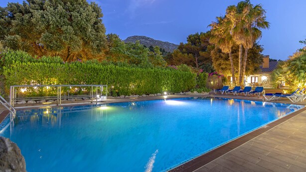 Ein Pool mit Liegestühlen, umgeben von Grünflächen und einem Berg im Hintergrund.