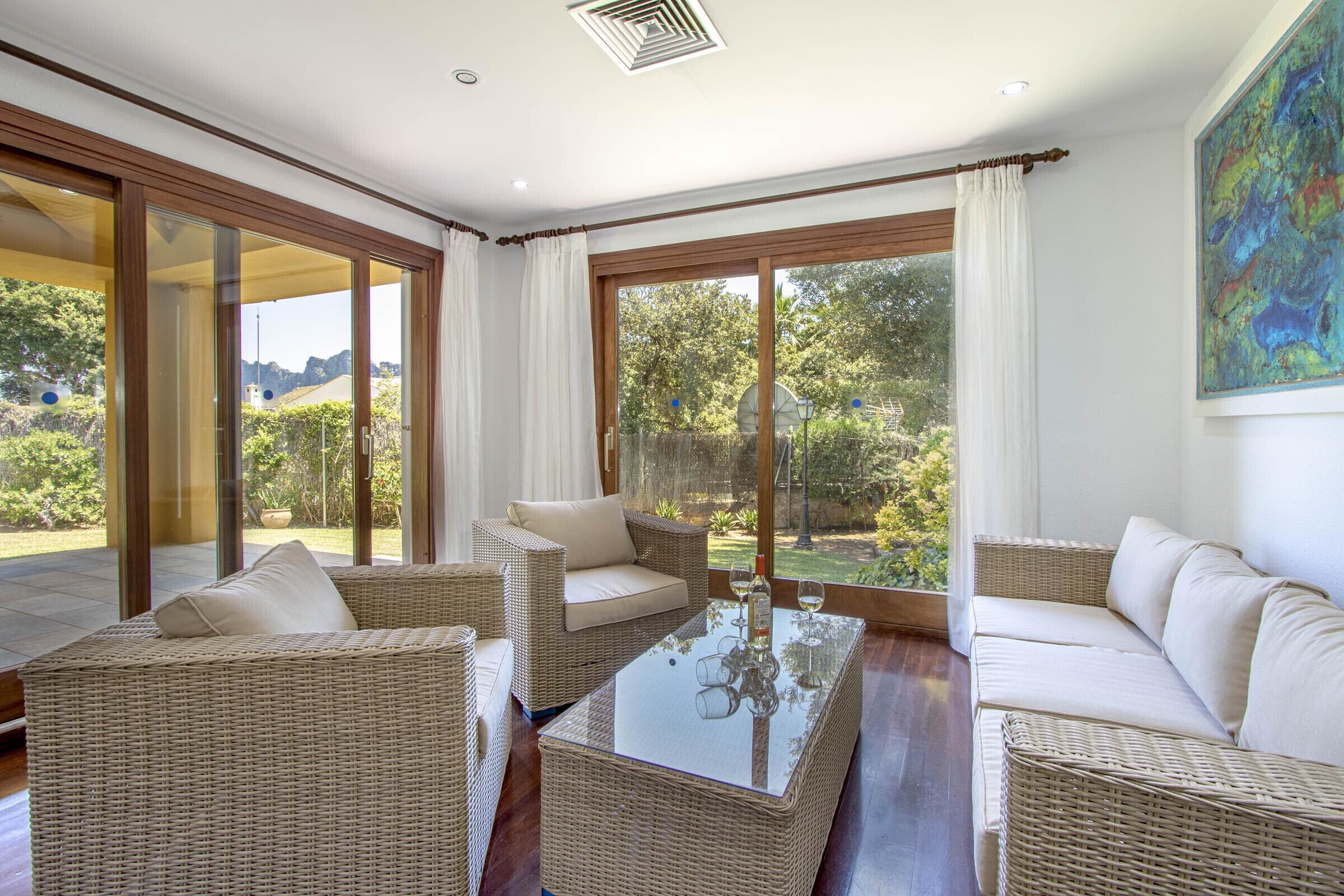 A spacious room with wicker furniture, large windows, and a view of greenery.