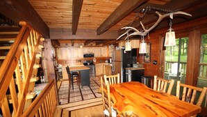 Un intérieur rustique en bois, avec une grande table à manger, des chaises en bois, un coin cuisine doté de meubles en bois et un luminaire suspendu fabriqué à partir de bois de cerf.