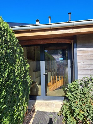 Une maison moderne avec une façade en bois, une porte en verre et un escalier apparent menant à une terrasse en bois.