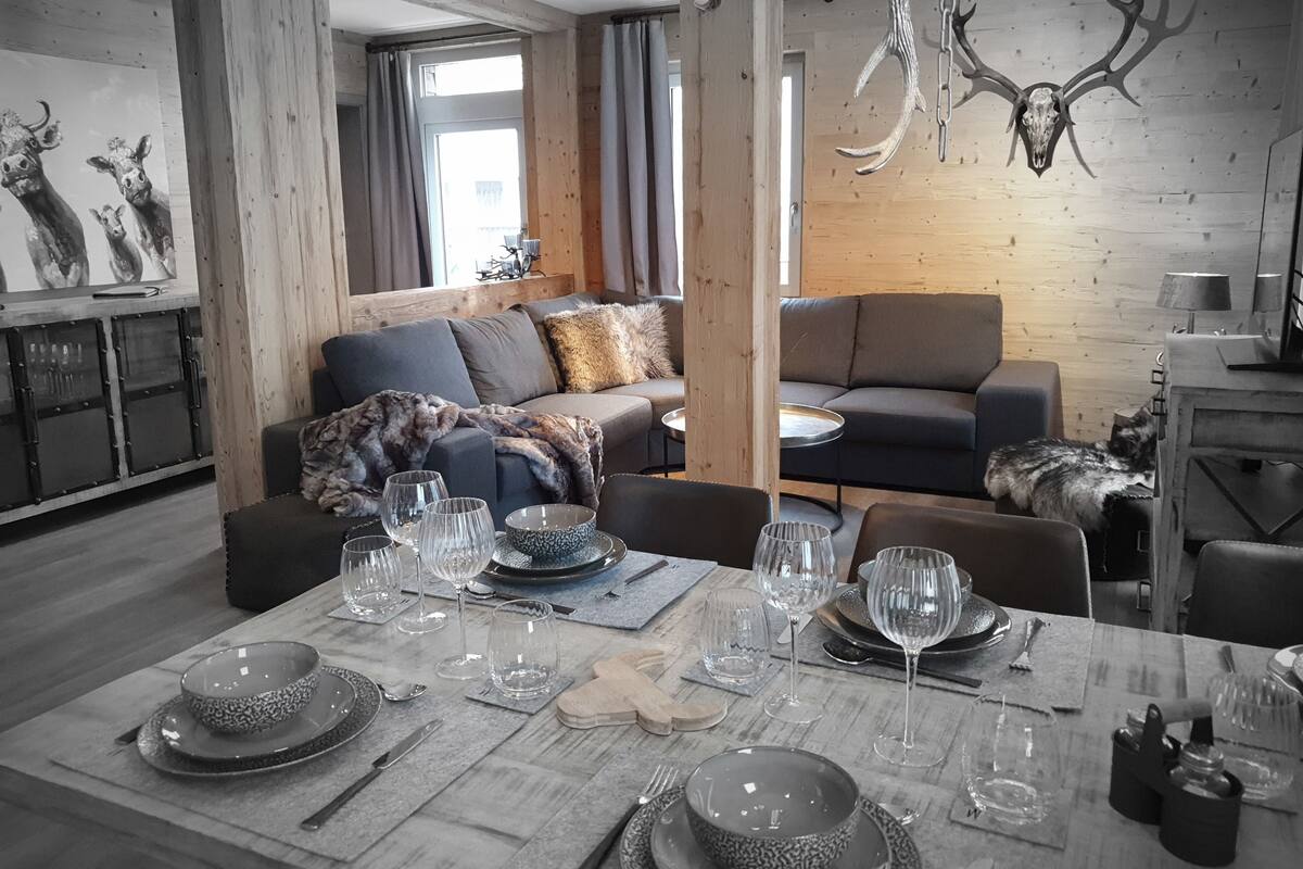 A modern living room with a dining area, wooden walls, and a chandelier.