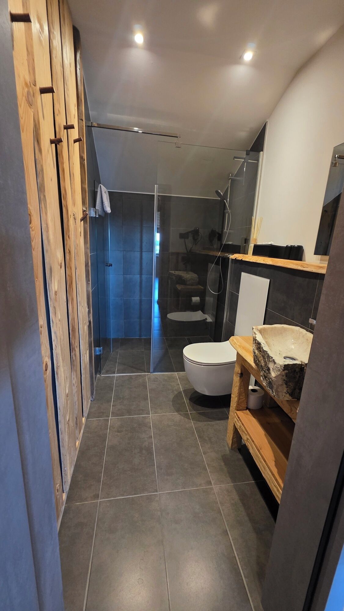 Un bagno moderno con box doccia in vetro, un water e un lavandino con ripiano in legno rustico.