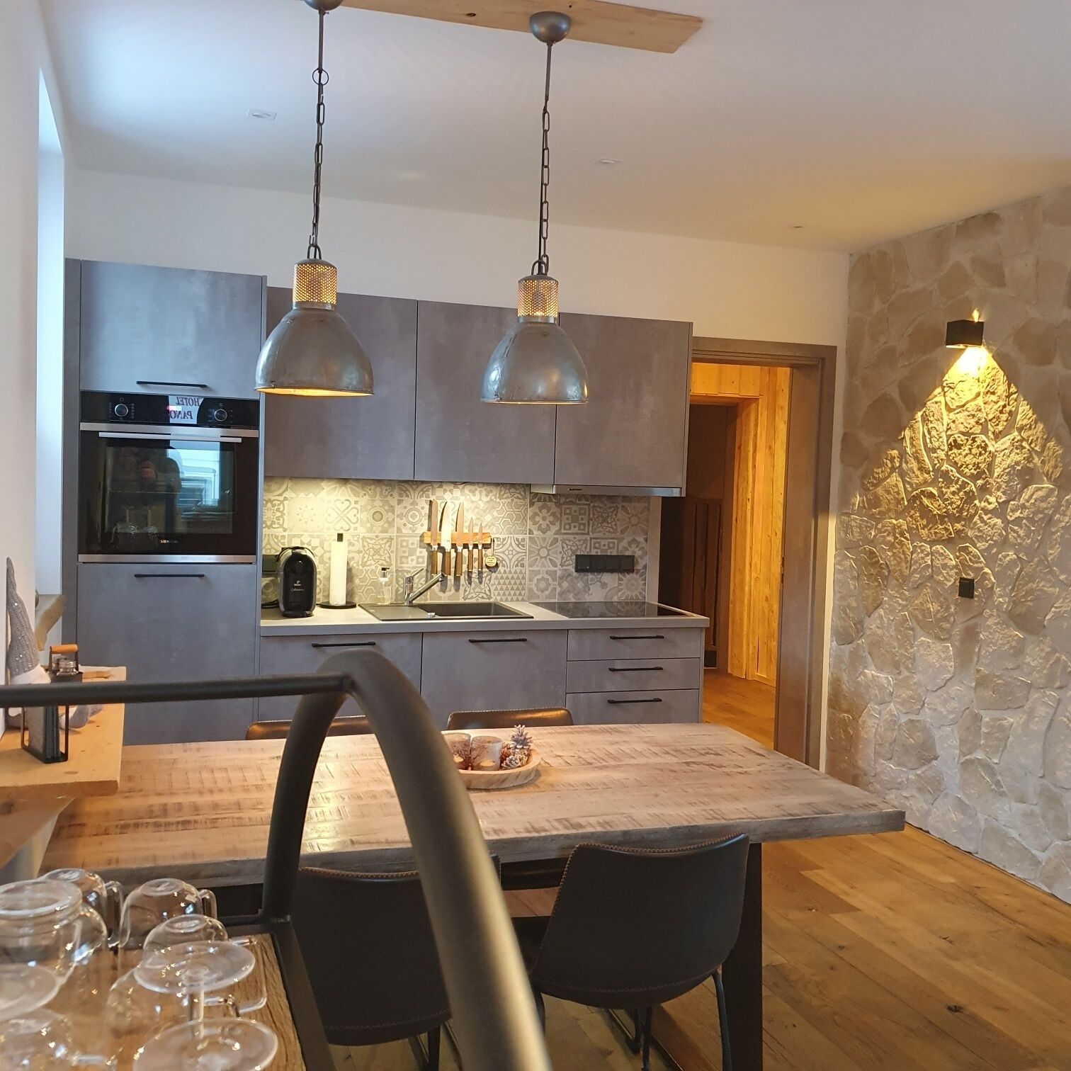 A modern kitchen with a central island, pendant lights, and a stone accent wall.