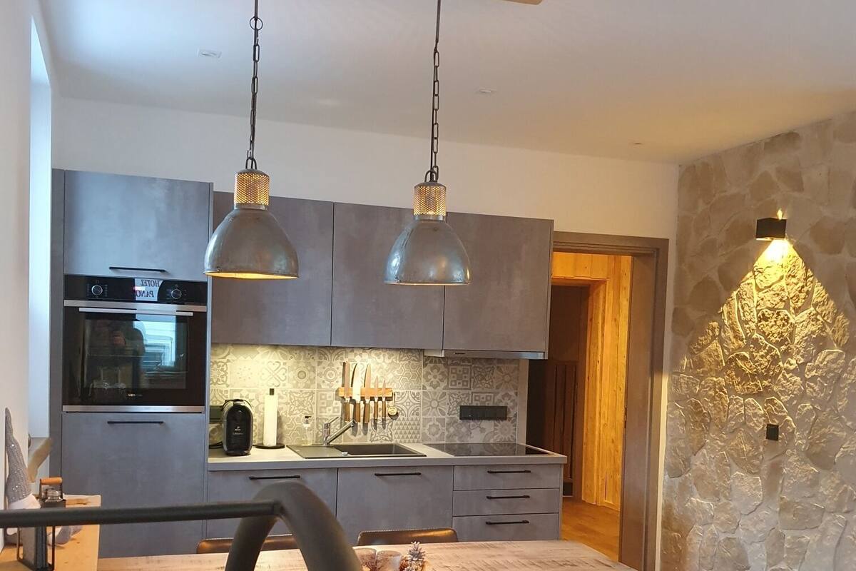 A modern kitchen with a central island, pendant lights, and a stone accent wall.