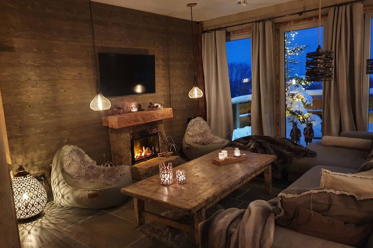 A cozy living room with a fireplace, comfortable seating, and a large window with a view of the outdoors.