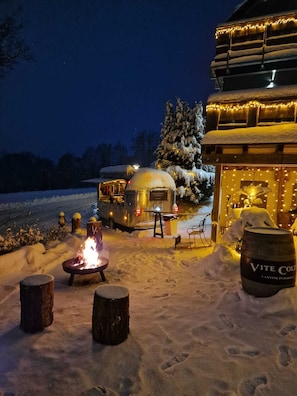 A snow-covered outdoor area with a fire pit, a wooden barrel, and a snow-covered tree. - WLodgeOne (Braunlage)