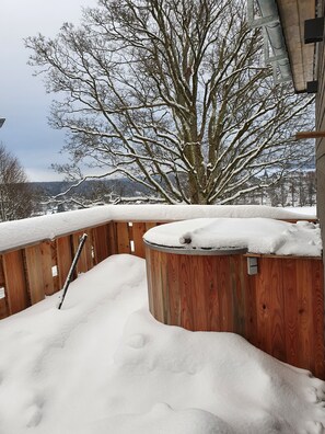 A wooden hot tub surrounded by snow, with a wooden fence and a tree in the background. - WLodgeOne (Braunlage)