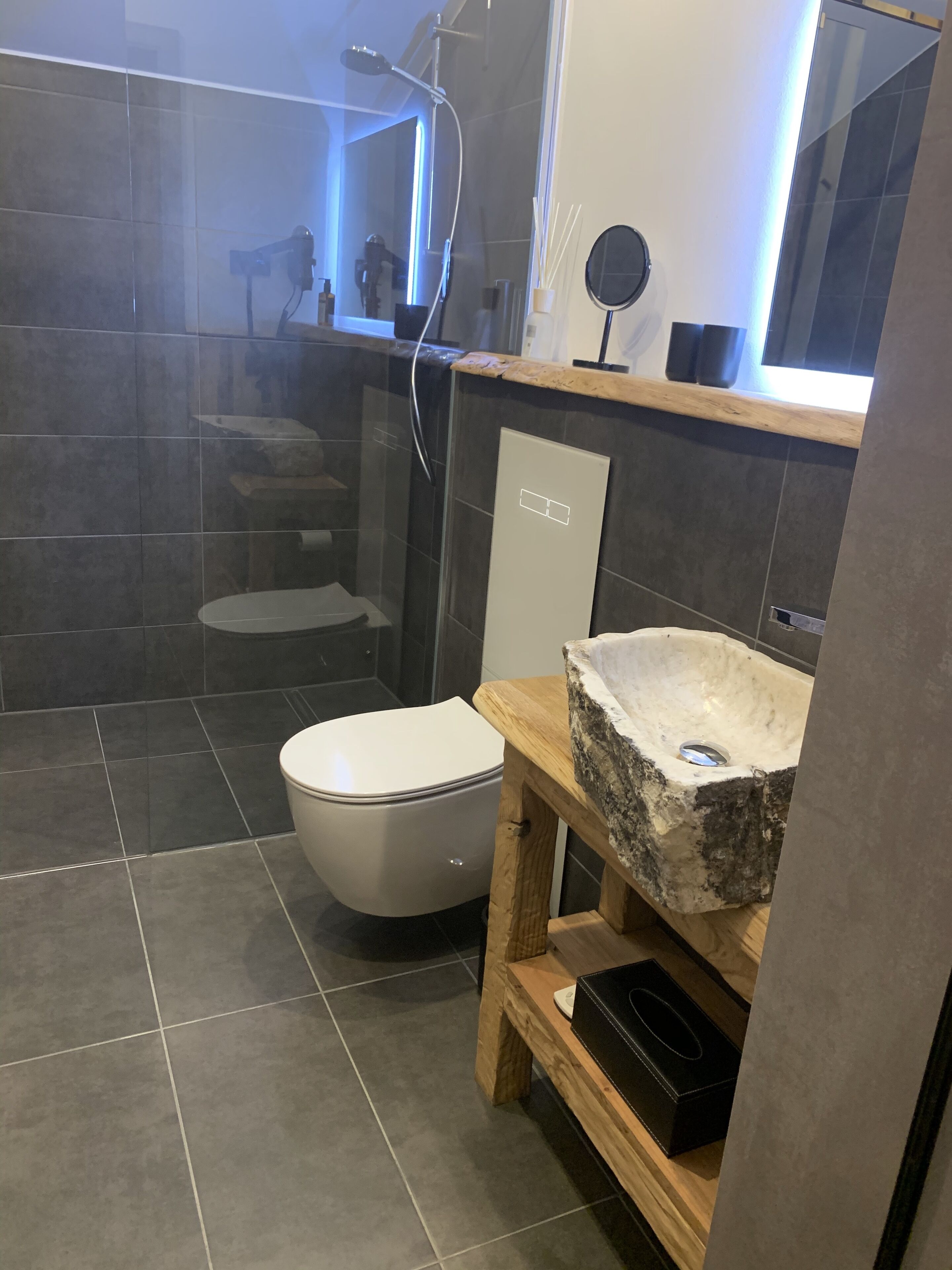 Une salle de bain moderne avec des toilettes, un lavabo en pierre et une douche séparée par une paroi de verre.