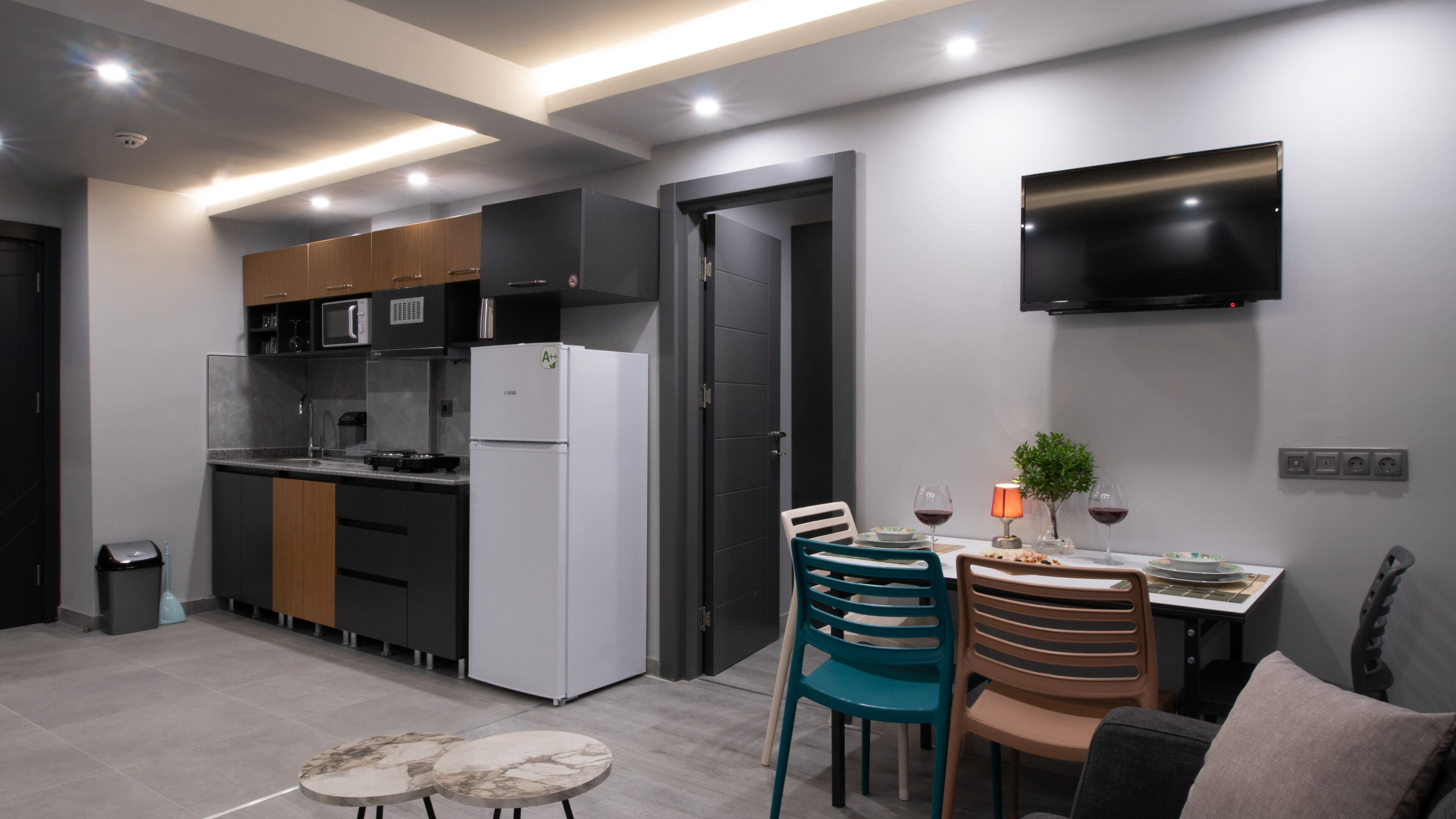 Eine moderne Küche mit integriertem Mikrowellenherd, Backofen und Kühlschrank. Ein Essbereich mit Tisch und Stühlen sowie ein Flachbildfernseher an der Wand sind vorhanden.