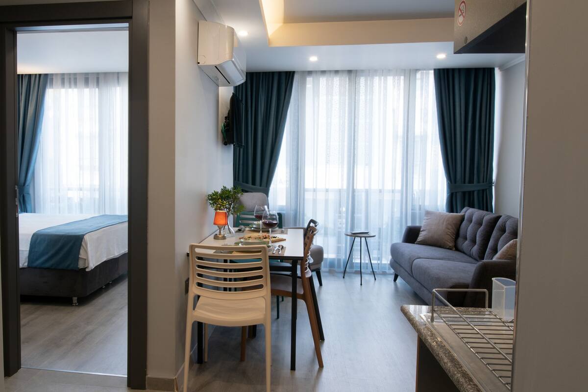 Una habitación de hotel moderna con una cama, una zona de comedor con mesa y sillas, un sofá y una mesita auxiliar.