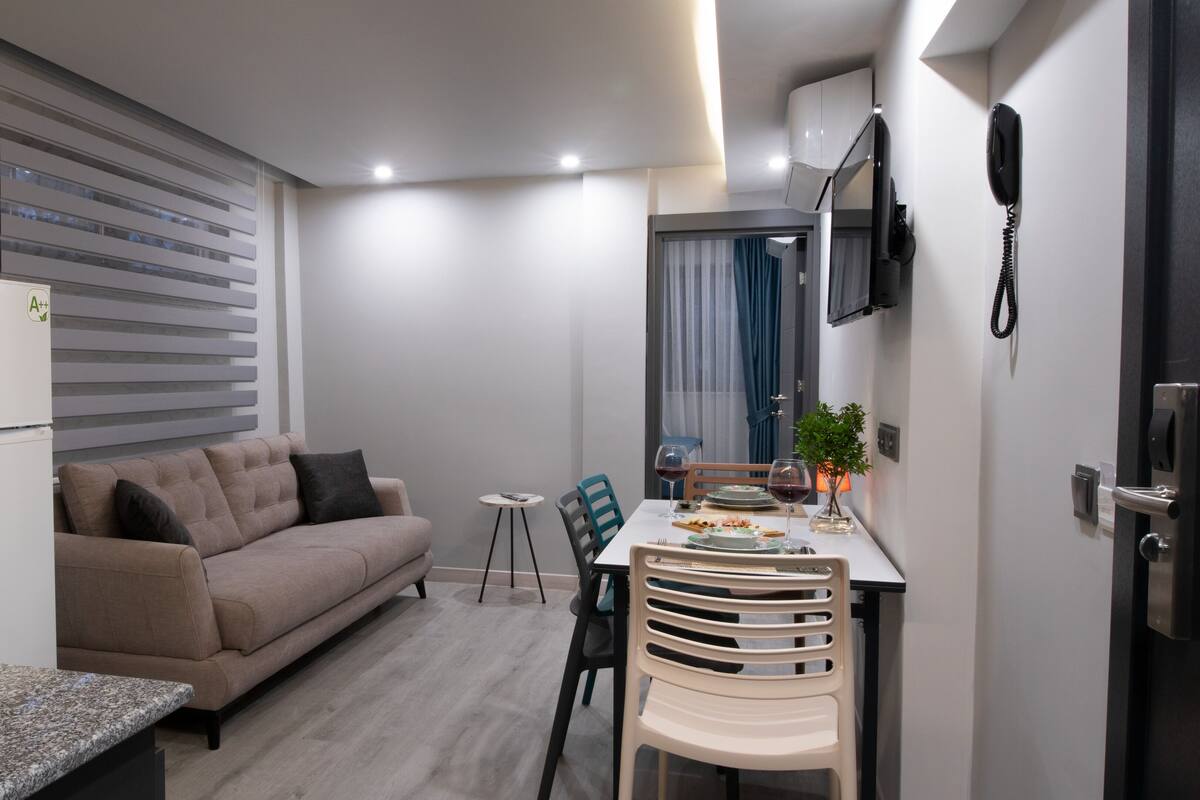Un espacio habitable compacto con kitchenette, un sofá, una mesa de comedor con sillas y un televisor montado en la pared.