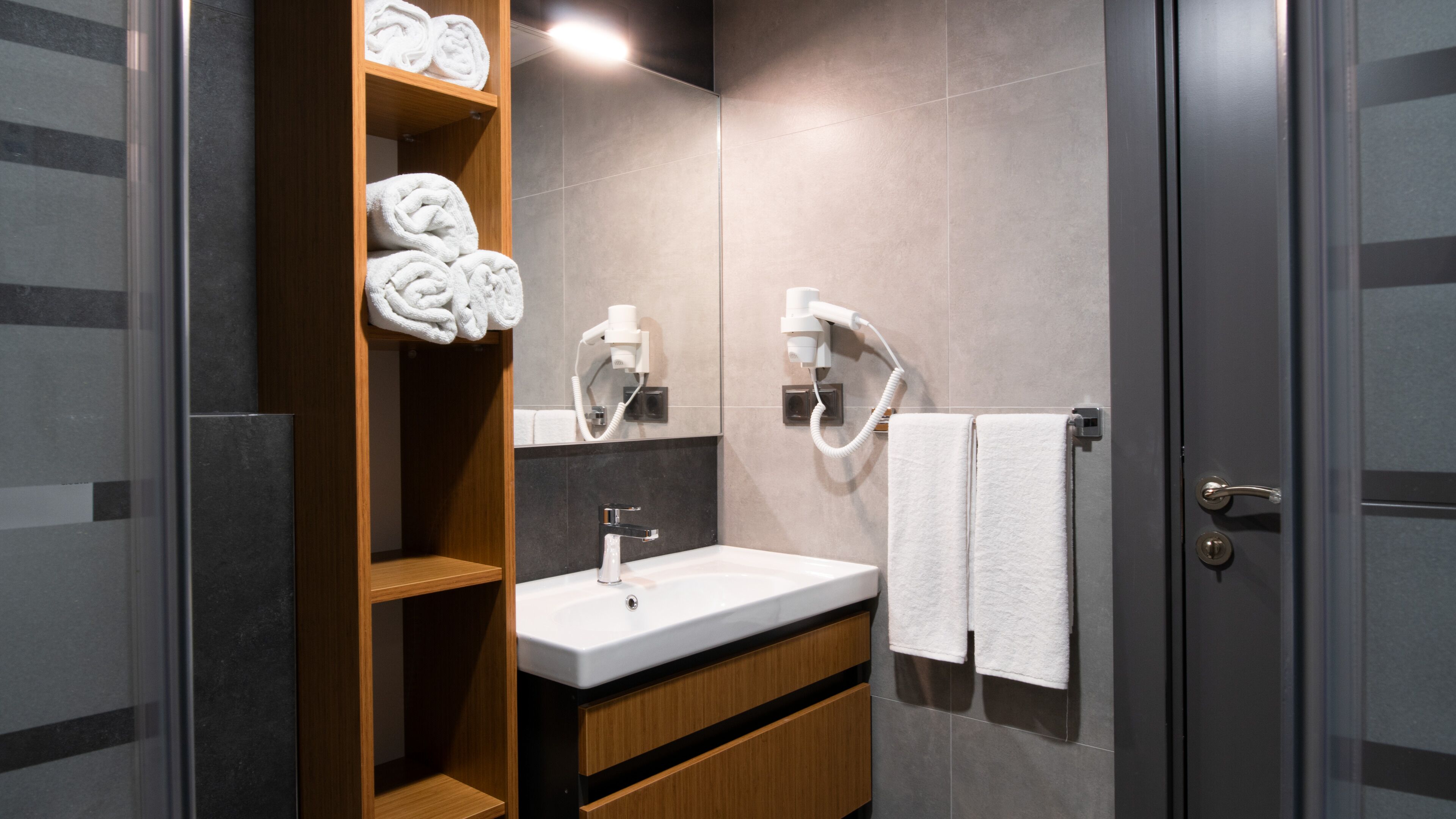 A modern bathroom with a wooden vanity, a sink, a mirror, and two towel racks.