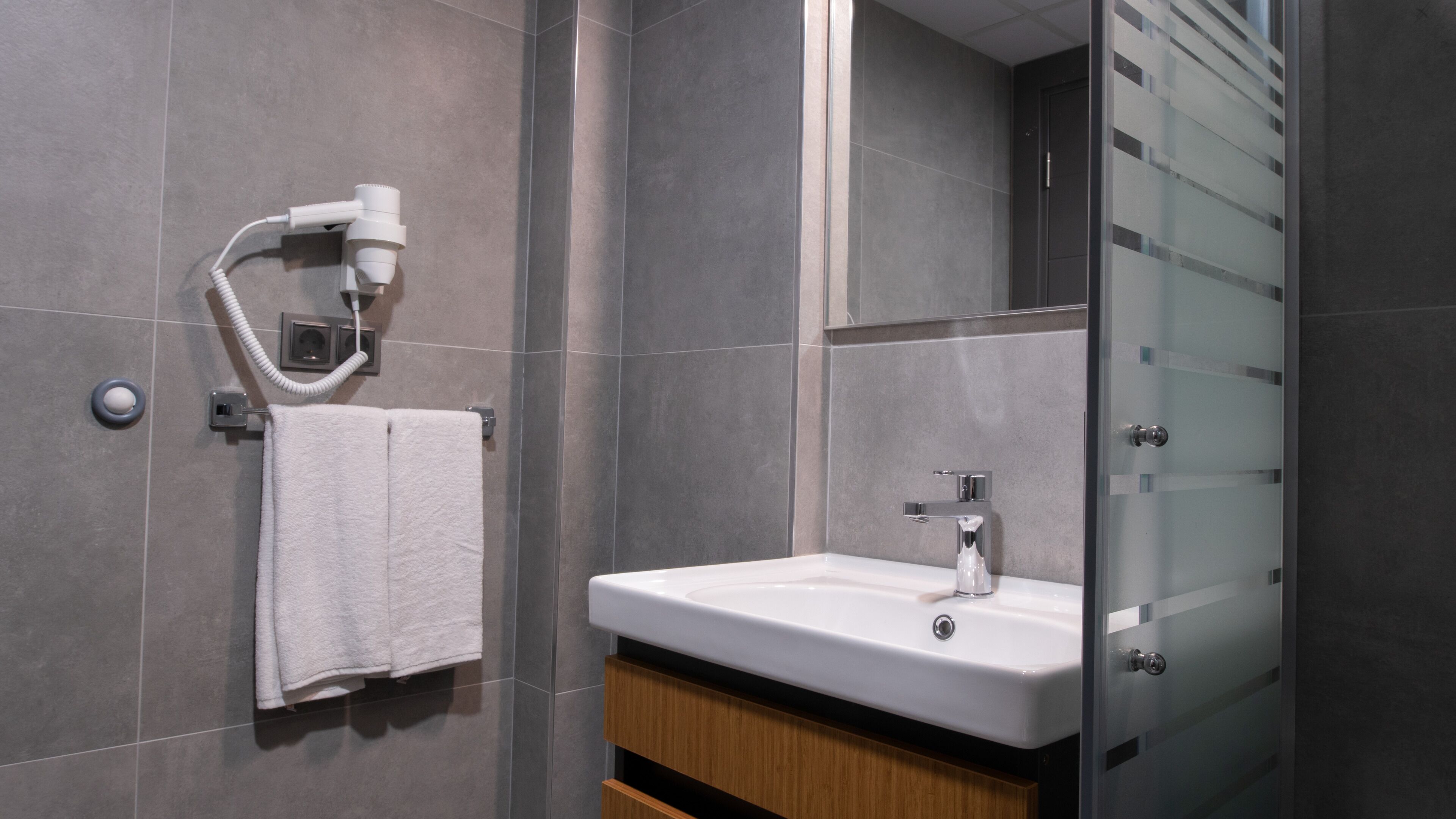 A modern bathroom with a white sink, a towel rack, a hairdryer, and a glass shower enclosure.